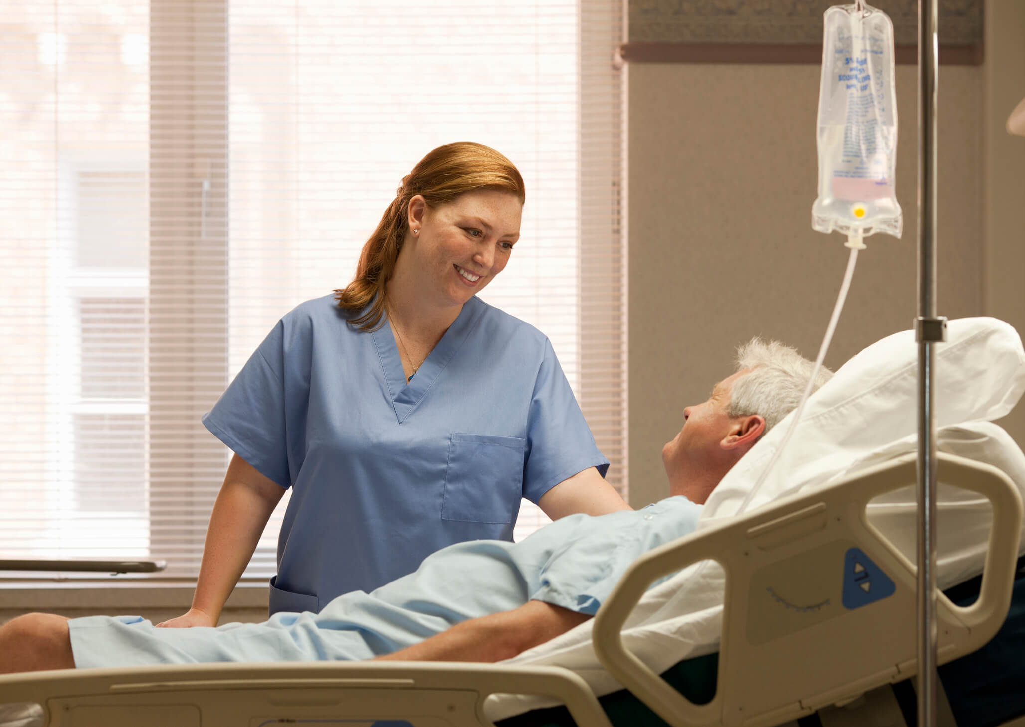 Smiling mid-adult female nurse checking in on an elderly male patient by his bedside in a hospital room