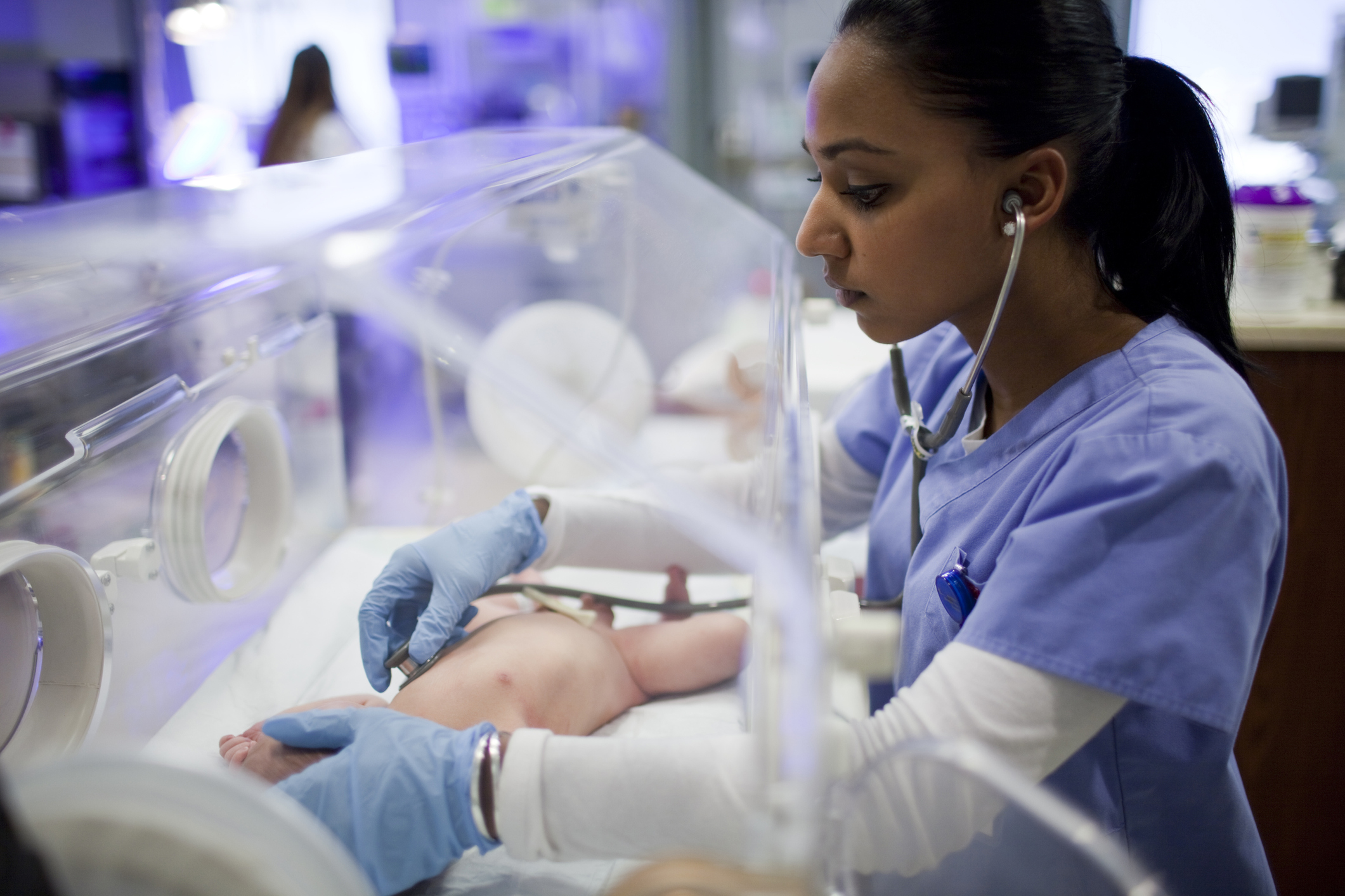 Nurse listening to heartbeat of newborn in incubator