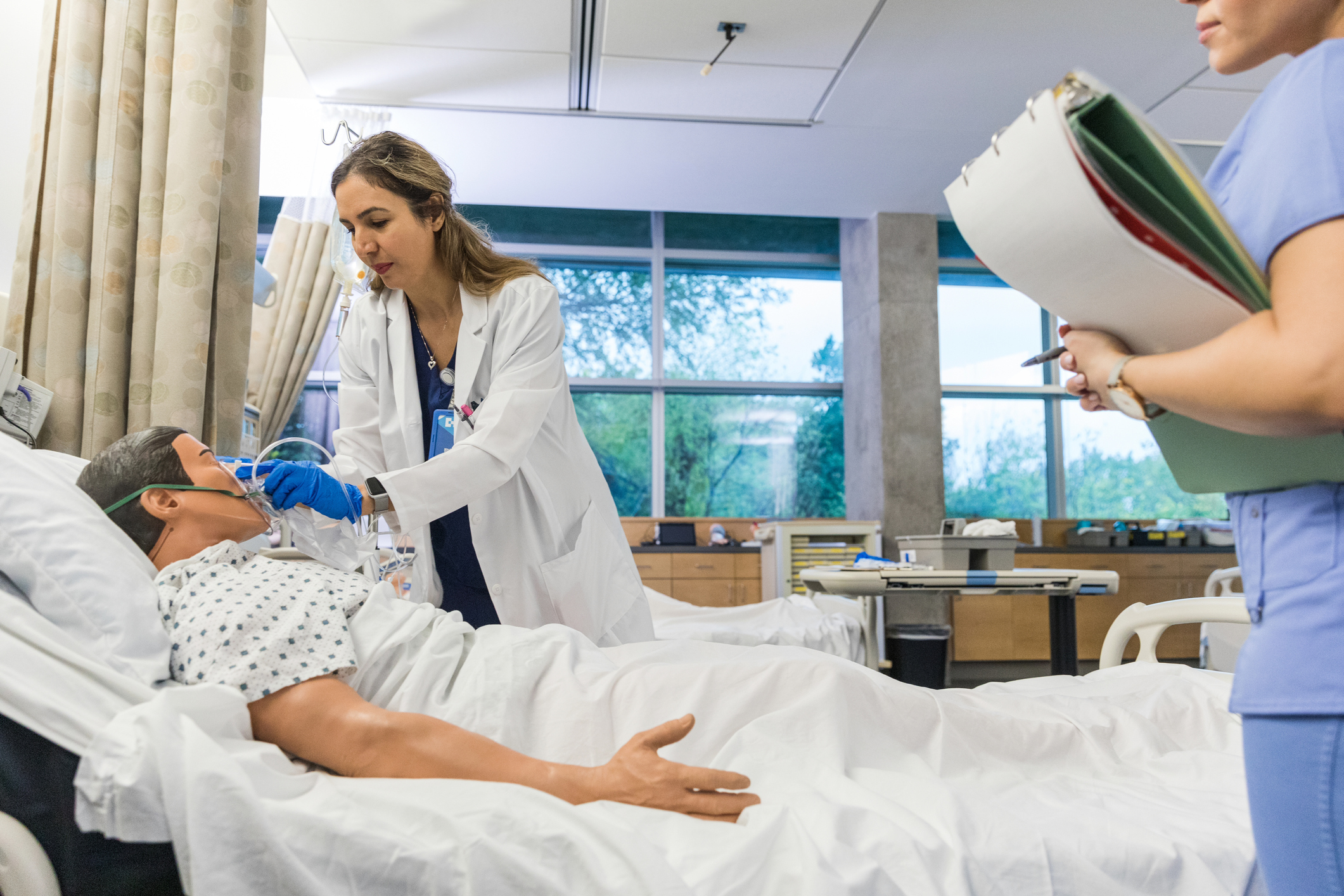 Nurse simulating patient care to a mannequin in hospital bed